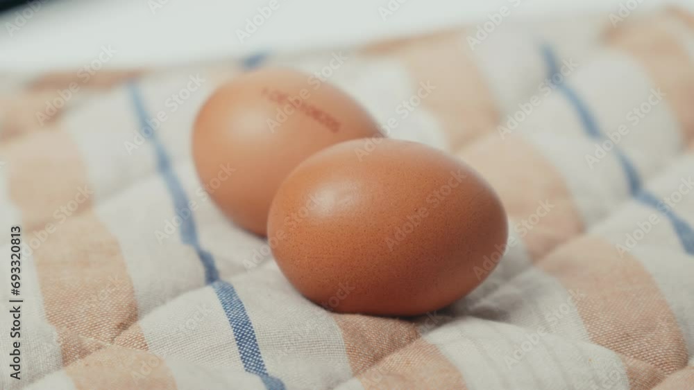 Two fresh brown eggs resting on a classic blue and white checkered kitchen towel. Two fresh brown eggs resting on a classic blue and white checkered kitchen towel.