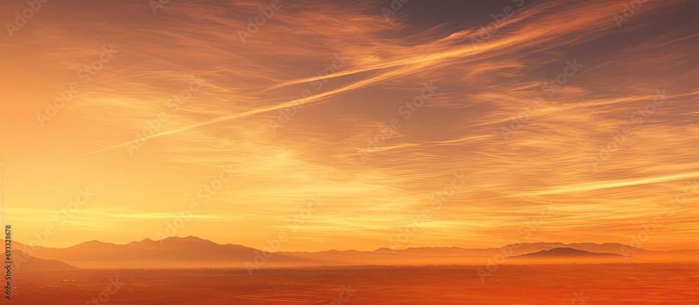 Vapor trails across orange sunset over landscape.