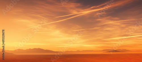 Vapor trails across orange sunset over landscape.