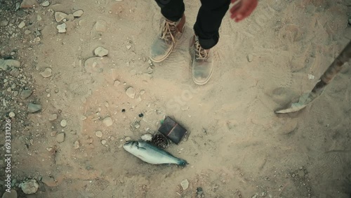 Person dropping a fish in the sand with a pine cone and a wallet. Slow motion photo
