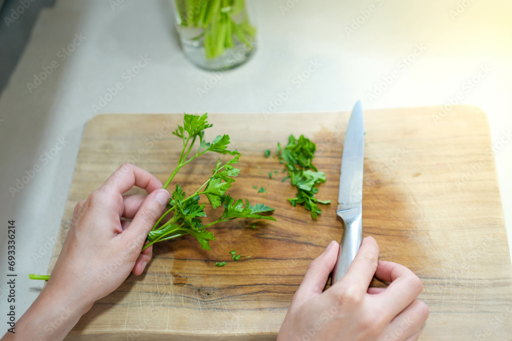 Top view of hands cutting with knife a branch of green healthy parsley spice in a wooden cutting board