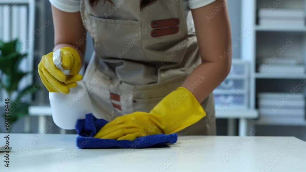 The young housekeeper wore gloves and cleaned the work table with a rag and cleaning spray. Professional office home cleaning products Providing hygiene services Free from germs. The young housekeeper wore gloves and cleaned the work table with a rag and cleaning spray. Professional office home cleaning products Providing hygiene services Free from germs.