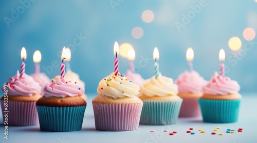 Birthday cupcakes with colorful candles on a pastel blue background.