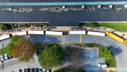 Students exiting American high school after school day. Yellow buses waiting to transport kids. Top down aerial descending shot.