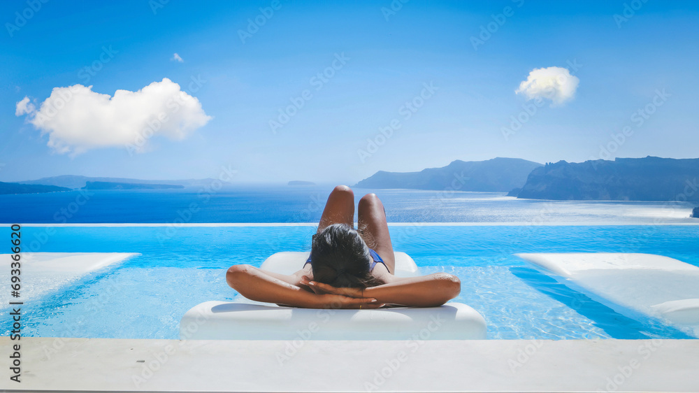 Young Asian women on vacation at Santorini relaxing in a swimming pool looking out over the Caldera ocean of Santorini, Oia Greece, Greek Island Aegean Cyclades during summer in Europe - obrazy, fototapety, plakaty 