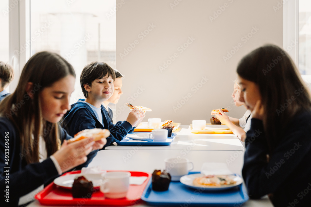 Group of school children having lunch while sitting in school cafeteria