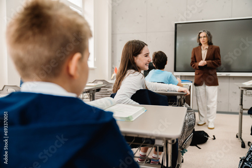 Portrait of school girl turning back and talking to classmate while sitting in classroom