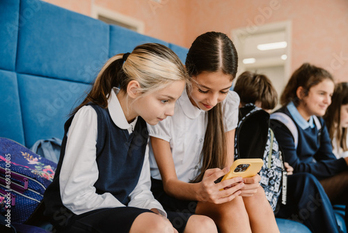 Primary school girls using smartphone while sitting in school lobby photo