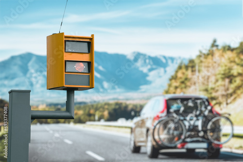 A radar-equipped speed camera monitors the traffic on a road, flashing a yellow light when it catches a car exceeding the speed limit, and using technology to identify the vehicle and enforce the law. photo