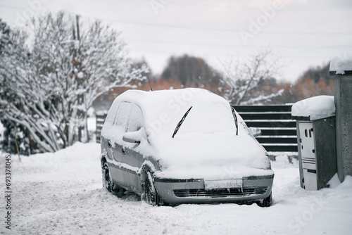 A car parked outdoors in winter is covered with snow and ice. The wiper blades are lifted up to prevent them from freezing to the windshield. The owner will need a scraper and a spray to clear glass