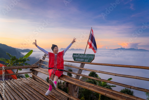 Asian traveler woman wearing a Red Karen Dress is happy with beautiful sea mist in the morning of mountain peaks the Thai language sign means Glor Selo Viewpoint of Mae Hong Son, Thailand. photo