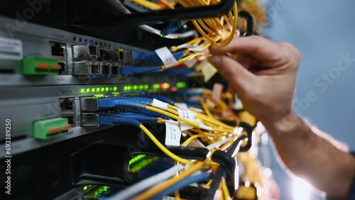 Close up view of hand that fixing internet. Young man is working with equipment and wires in server room photo