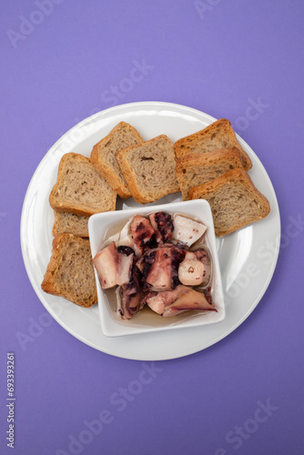 octopus salad with oil in small bowl and toasts photo