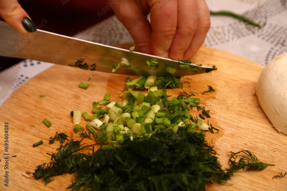 Crop anonymous female chef in uniform cutting fresh green parsley with knife on cutting board in kitchen Crop anonymous female chef in uniform cutting fresh green parsley with knife on cutting board in kitchen