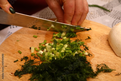 Crop anonymous female chef in uniform cutting fresh green parsley with knife on cutting board in kitchen