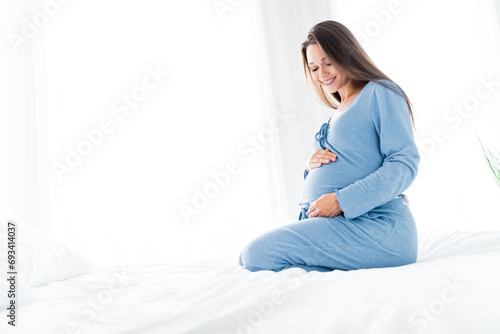 Photo of pretty charming young mom nightwear sitting bed talking baby belly indoors house room