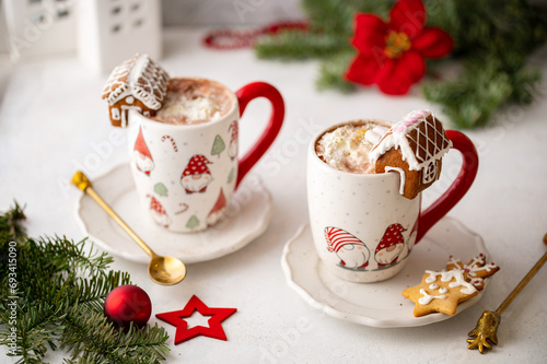 Winter hot chocolate with marshmallows in a mug with marshmallow on a light background. Cozy still life with cocoa drink, cookies and decorations, gingerbread house, fir branch and poinsettia.