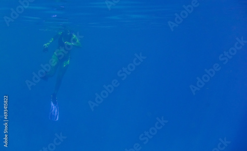 woman in bikini and fins snorkeling in deep blue water