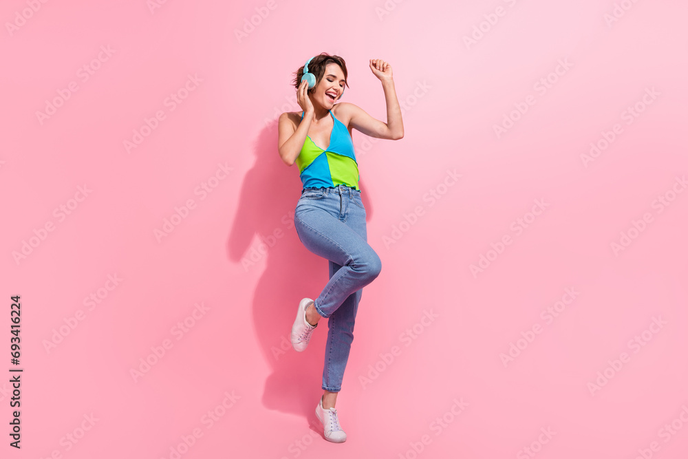 Full length cadre of charming hipster lady dance carefree touching her blue wireless earbuds loud sound isolated on pink color background Full length cadre of charming hipster lady dance carefree touching her blue wireless earbuds loud sound isolated on pink color background