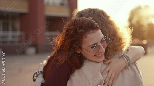 Cheerful student girl hugs her friend near the school photo