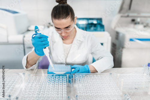 Young woman scientist working conducts research in modern bio laboratory. Female doctor laboratory assistant do tests, taking samples from test tubes with pipette