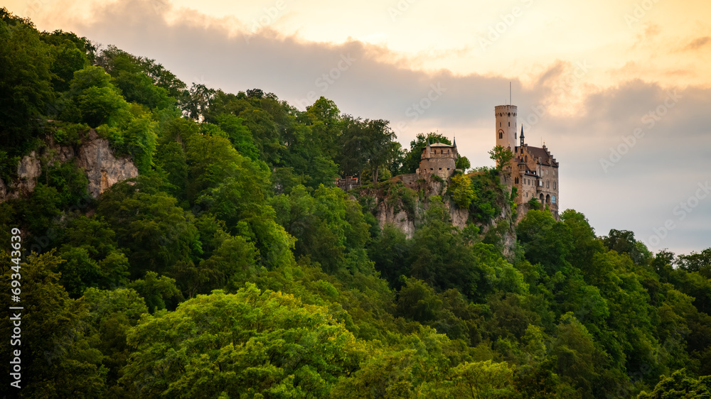 Panoramic view with Lichtenstein Castle located in Swabian Jura of southern Germany on a steep cliff overlooking the Echaz valley near Honau Reutlingen with warm sunset atmosphere on a summer evening. - obrazy, fototapety, plakaty 