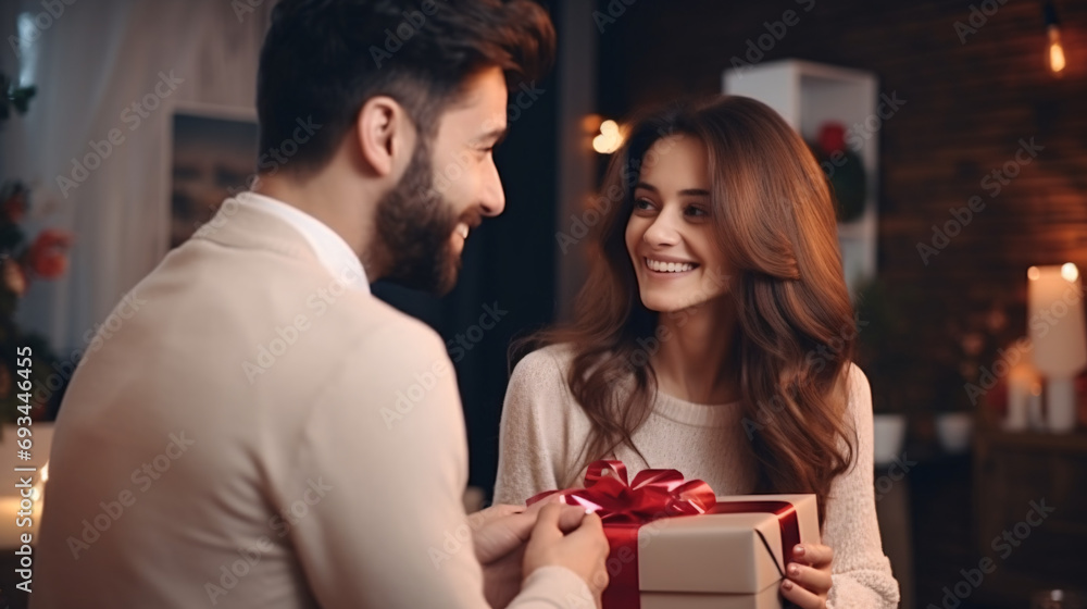 Beautiful young couple holding gift box and looking at each other while celebrating Christmas at home Beautiful young couple holding gift box and looking at each other while celebrating Christmas at home