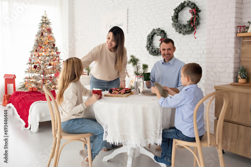 a family in a kitchen decorated for Christmas drinks cocoa with marshmallows and eats pie. parents with their daughter and son talking cheerfully in a large  beautiful kitchen.