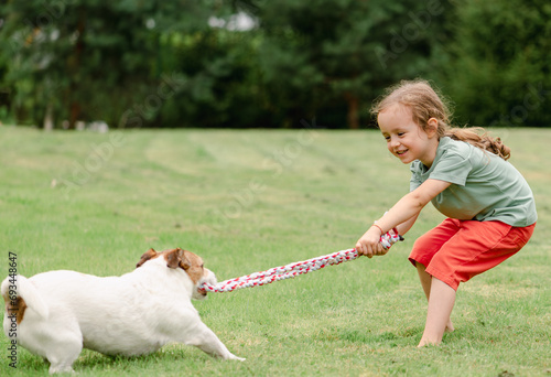 Child and dog playing tug with toy rope at backyard lawn