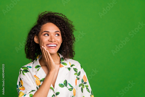 Photo portrait of pretty young girl touch cheek look empty space dressed stylish orange print outfit isolated on green color background