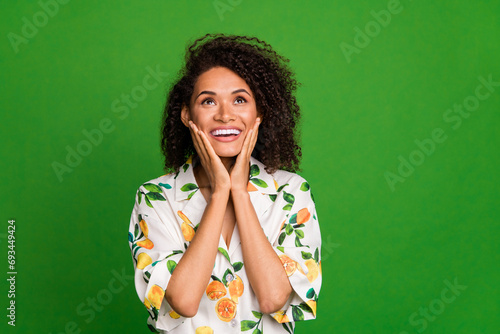 Photo portrait of lovely young lady touch cheeks look up admire dressed stylish orange print garment isolated on green color background