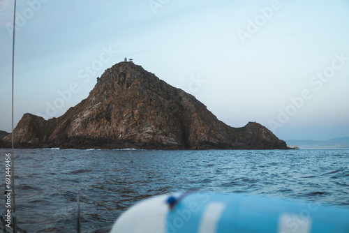 Summer evening from a sailboat, glimpse the blurred paddleboard, deep blue Atlantic waters, and the rocky cliffs of Montefaro on the Cíes Islands, bathed in soft post-sunset light. photo