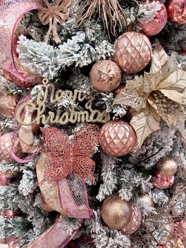 pink rose gold snow christmas tree decorations detail close up with baubles balls and glitter festive ribbon and merry christmas lettering text