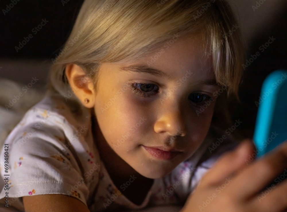 Blonde child/girl using her mobile phone just before sleeping, to watch a video. Blonde child/girl using her mobile phone just before sleeping, to watch a video.