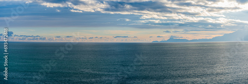 Wide-screen panorama of the sea and mountains with feathery clouds, a high-angle view. © Provokator