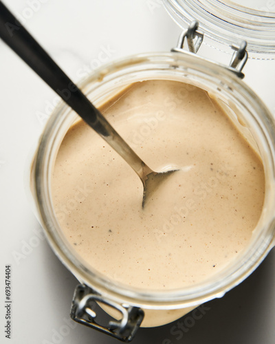 Tarator - Lebanese sauce from tahini with garlic, lemon juice and water. White or cream colored sauce in a jar on a marble background