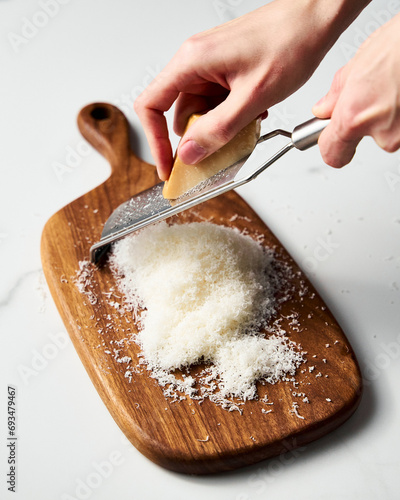 Man hands grating parmesan cheese on a wooden board. White, bright and clean background.