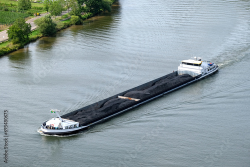 Konzept Schiffsverkehr und Warentransport auf einem Fluss: Blick von oben auf einen mit Erz beladenen Frachter auf der Mosel in Deutschland, mit Ufer und Copy Space