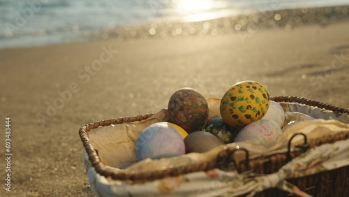 Wicker basket with Easter eggs on the beach by the sea. Close-up, sun rays and waves.