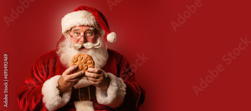 Christmas Santa Claus Eating a Giant Cookie on a Red Background with Space for Copy photo