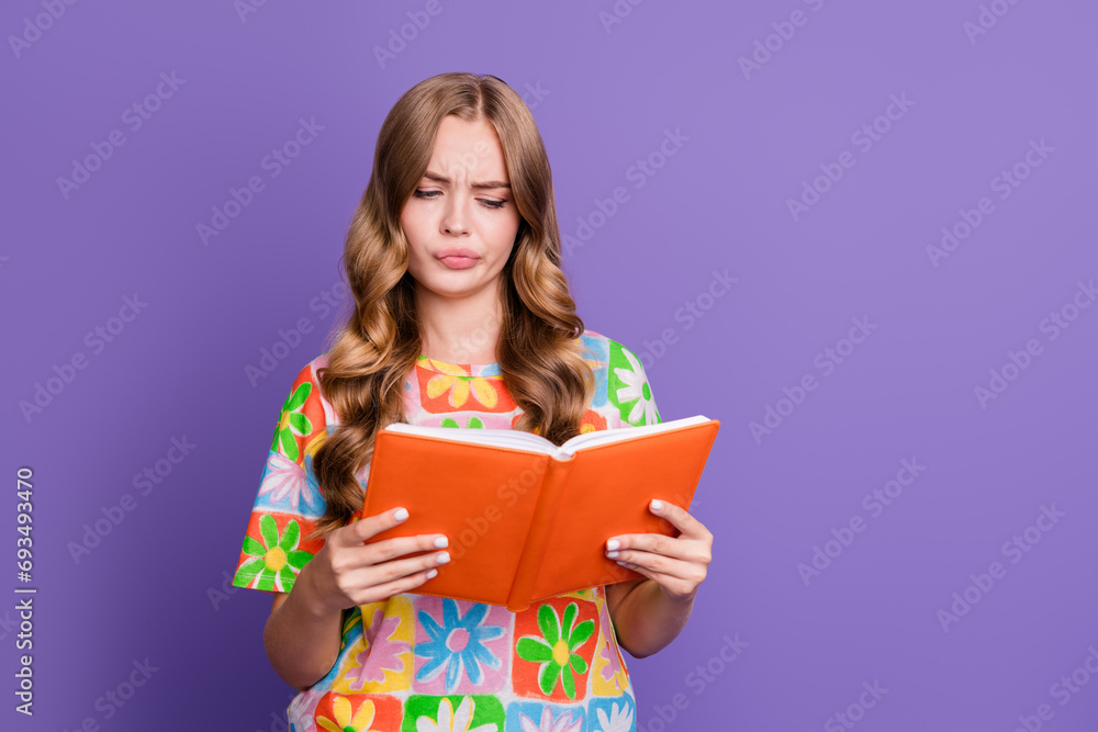 Photo of minded clever student with wavy hair wear print t-shirt thoughtfully look at book in arms isolated on purple color background Photo of minded clever student with wavy hair wear print t-shirt thoughtfully look at book in arms isolated on purple color background