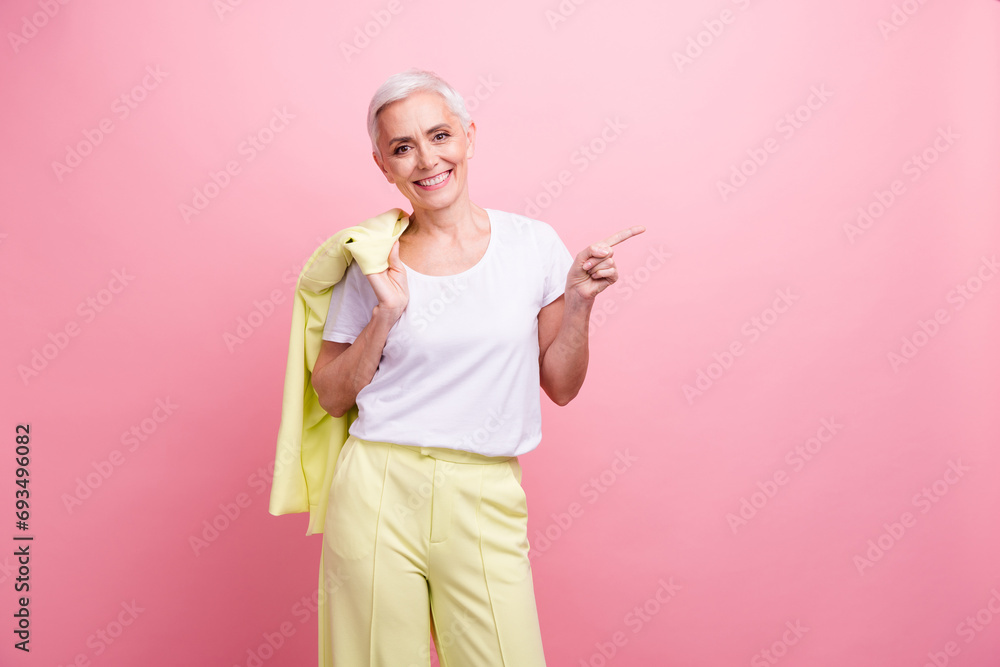 Photo of happy smiling old woman in yellow suit bring her jacket direct finger corporation brand novelty isolated on pink color background Photo of happy smiling old woman in yellow suit bring her jacket direct finger corporation brand novelty isolated on pink color background