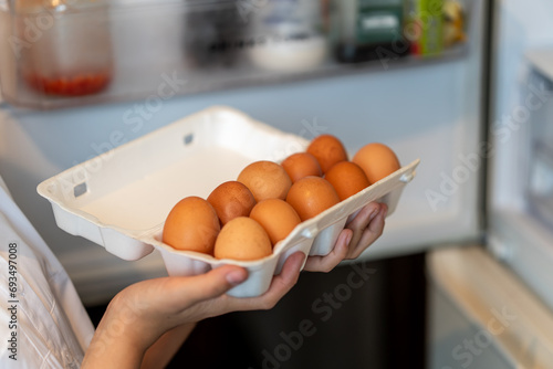girl takes fresh brown chicken eggs in a package from the refrigerator. Female hand lays chicken eggs from cardboard packaging in refrigerator