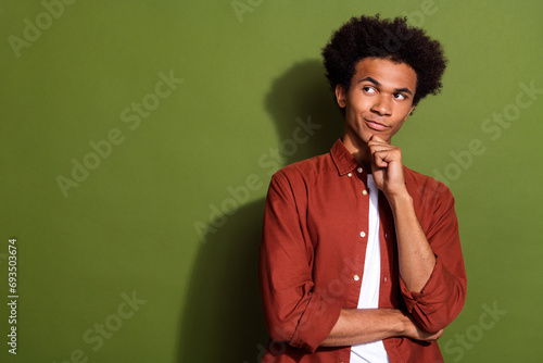 Photo portrait of attractive young man touch chin look tricky empty space dressed stylish brown clothes isolated on khaki color background