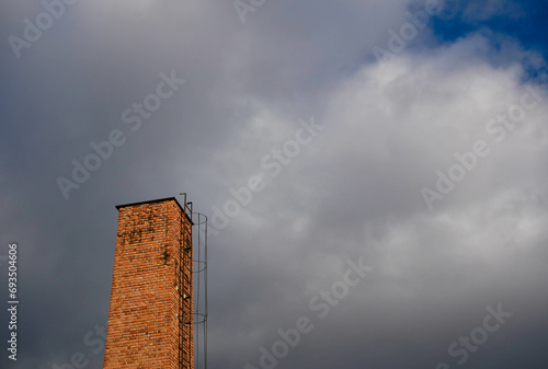 Old unused industrial chimney with a metal letter against cloudy winter sky.