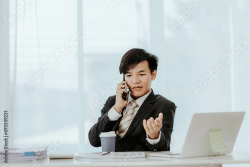 Asian male businessman working with laptop computer and smart phone with accounting documents at table in office Happy man working concept