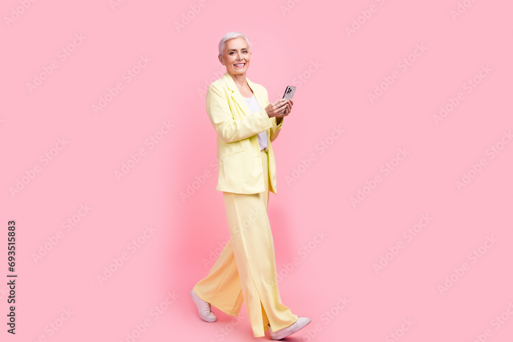 Full body photo of intelligent cheerful person dressed yellow jacket walk in empty space read email isolated on pink color background Full body photo of intelligent cheerful person dressed yellow jacket walk in empty space read email isolated on pink color background
