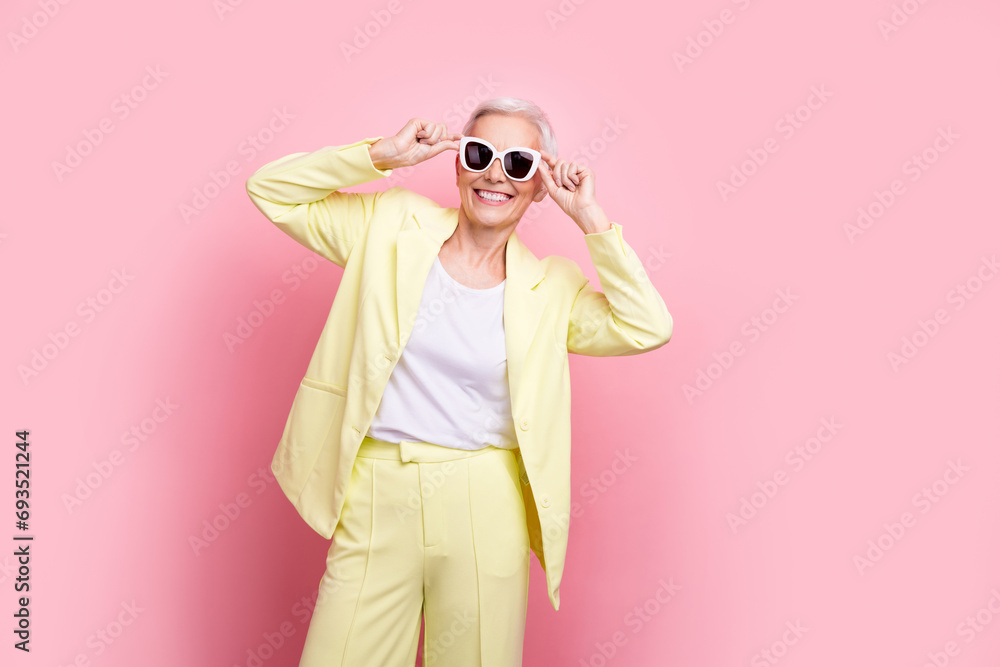 Photo of tourist aged lady yellow trendy suit trying new sunglasses posing for banner black friday sale isolated on pink color background Photo of tourist aged lady yellow trendy suit trying new sunglasses posing for banner black friday sale isolated on pink color background