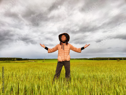 An adult girl looking like a cowboy in a hat in a field and with a stormy sky with clouds takes pictures of a rainbow and takes selfie in the rain. Woman having fun outdoors on rural and rustic nature © keleny