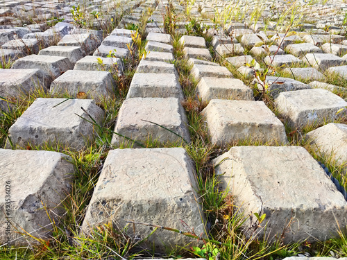 Rows of concrete cubes or rectangles on the bank of a river with grass. Breakwaters, protection from water in nature. Background, texture, location